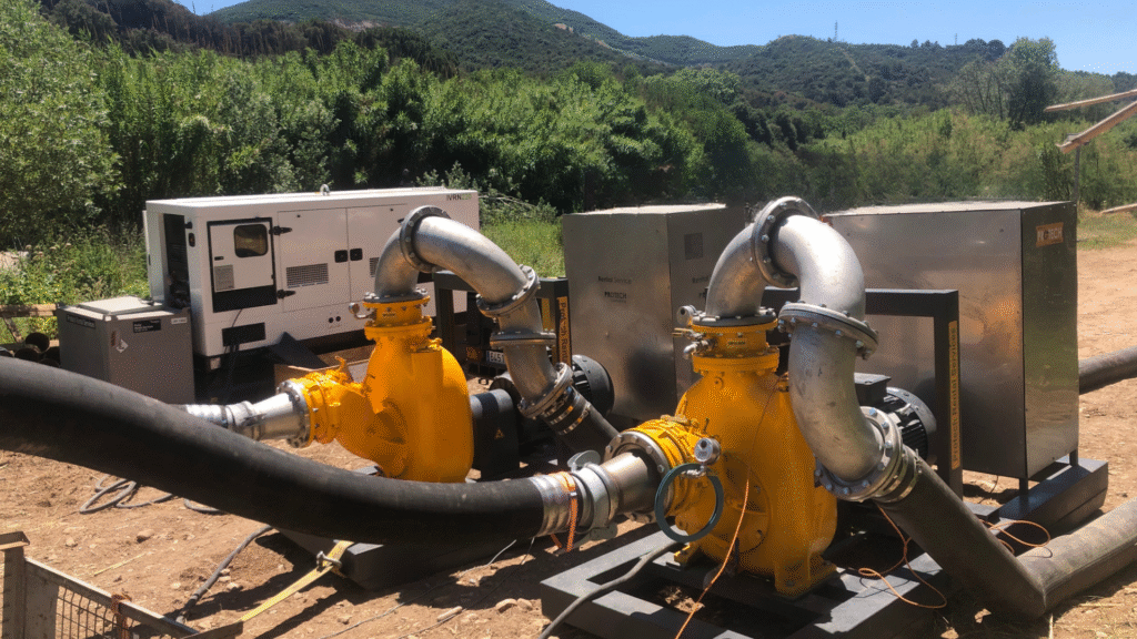 Bombas industriales autoaspirantes conectadas a mangueras, con generadores Protech Rental en un entorno natural para deshidratación de fangos.