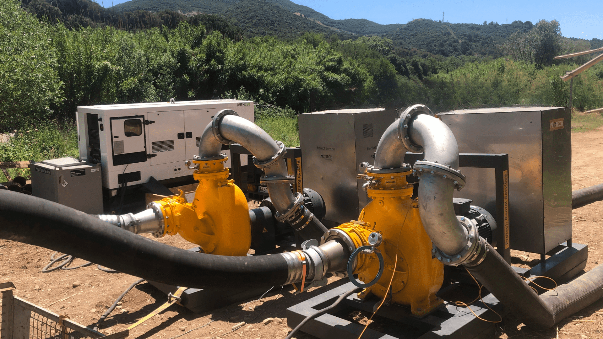 Bombas industriales autoaspirantes conectadas a mangueras, con generadores Protech Rental en un entorno natural para deshidratación de fangos.