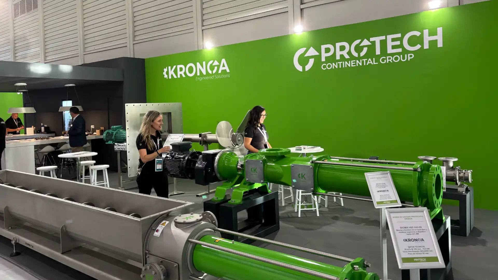 Stand de Protech Continental Group y Kronoa en una feria, con bombas industriales expuestas y dos personas atendiendo a los visitantes.