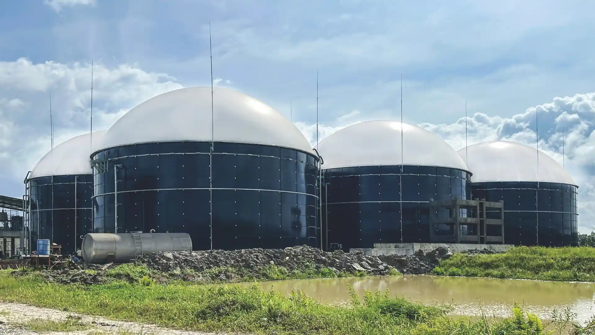 Vista exterior de una planta de biogás con grandes digestores y tanques industriales, rodeada de vegetación.