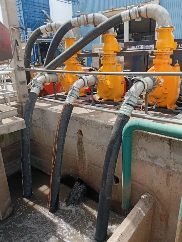 Industrial pump rental system at a wastewater treatment plant, with suction and discharge hoses for temporary pumping.